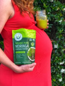 Pregnant woman in red dress with bag of moringa powder